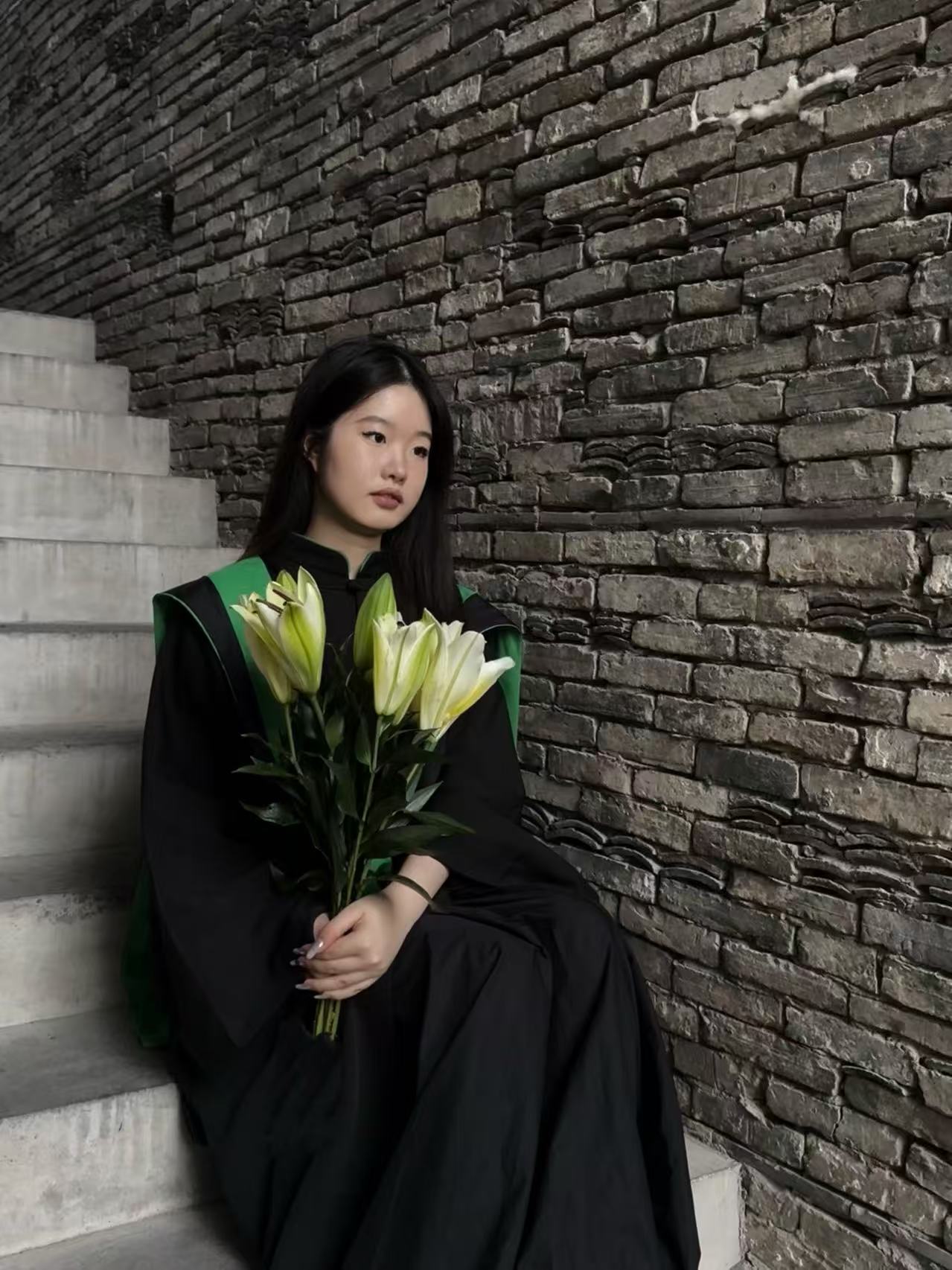 Portrait of Yiyi Qian seated beside a brick wall holding lilies